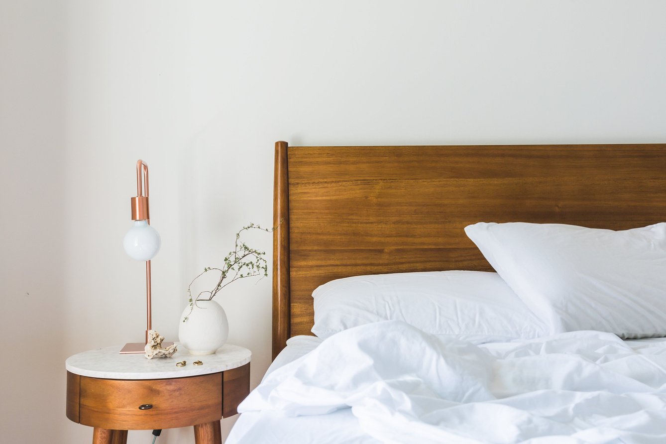 White Bedspread Beside Nightstand With White and Copper Table Lamp